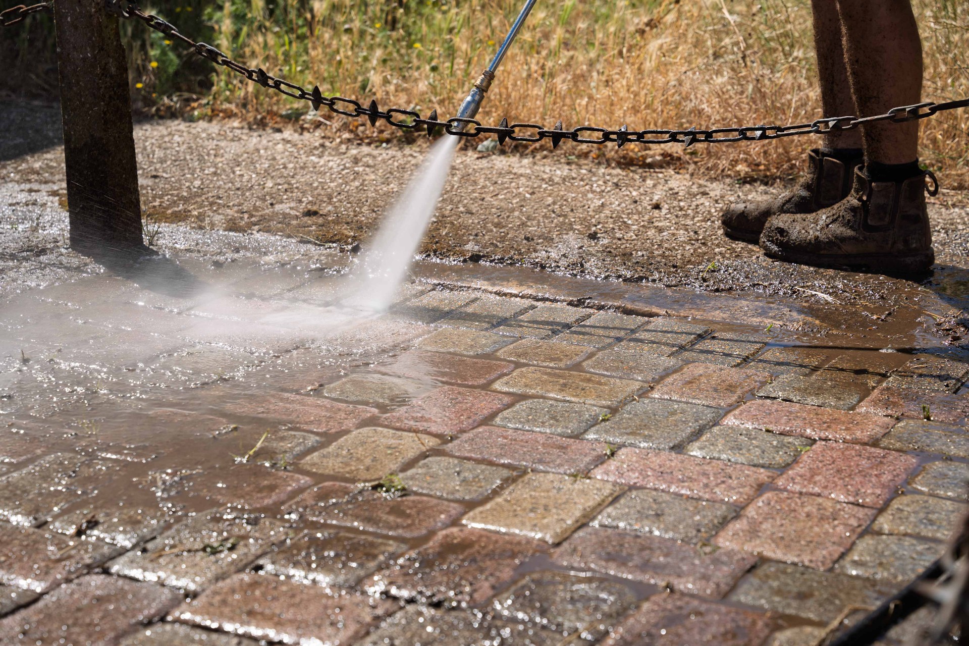 Close-up of a pressure washer spray lifting dirt from block paving